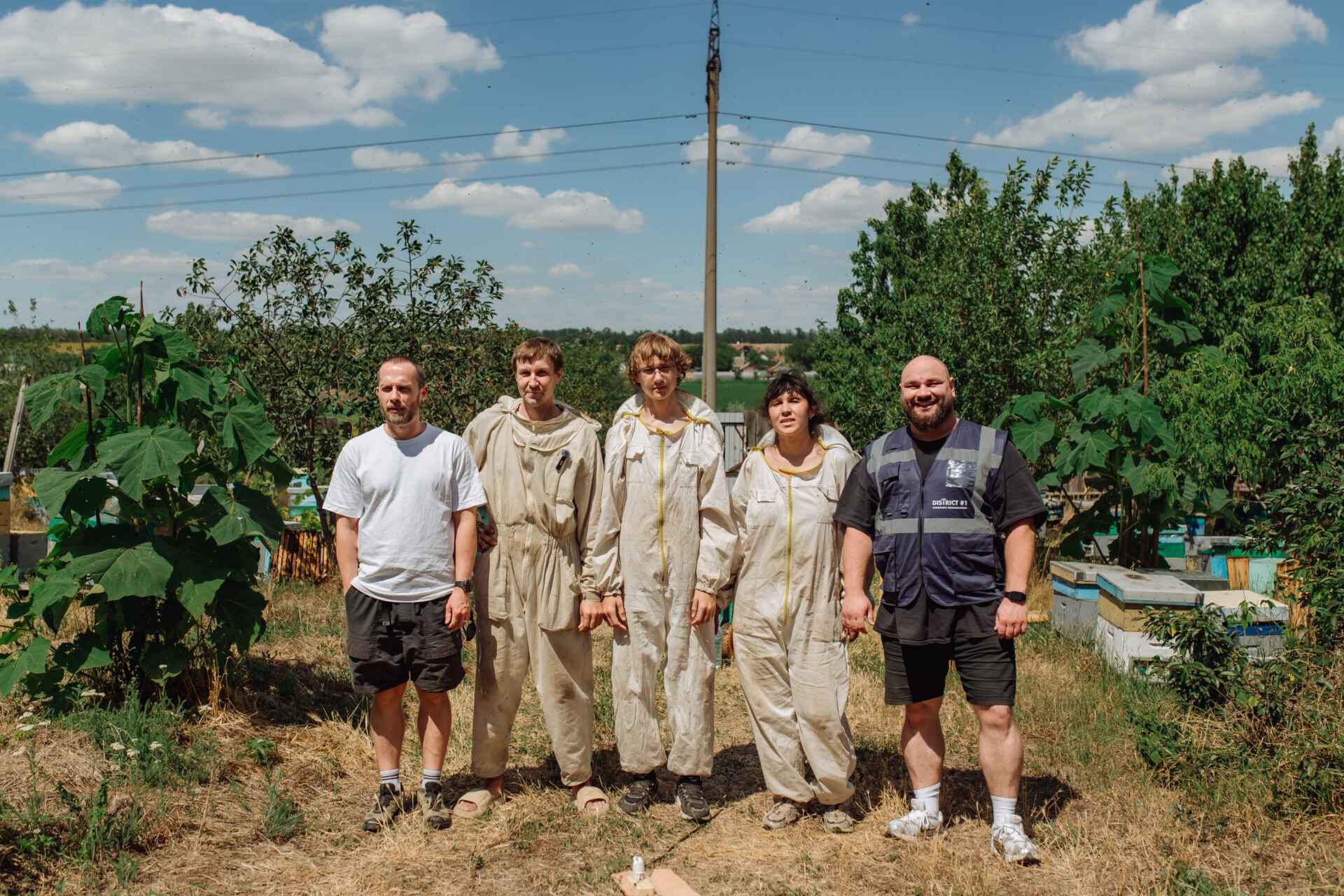 drei Imker*innen und zwei Helfer vor Binenstöcken in der Ukraine